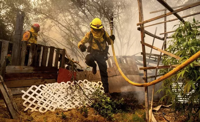 Firefighter Christian Moorhouse jumps over a fence while battling the Park Fire in the Cohasset community of Butte County, Calif., on Thursday, July 25, 2024. His crew was able to keep flames from reaching the mobile home they were protecting. (AP Photo/Noah Berger)