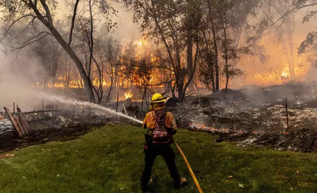 Cal Fire firefighter Christian Moorhouse defends a mobile home while battling the Park Fire in the community of Cohasset near Chico, Calif., Thursday, July 25, 2024. (Stephen Lam/San Francisco Chronicle via AP)