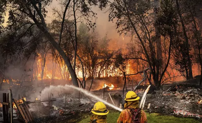 Firefighters spray water while battling the Park Fire in the Cohasset community of Butte County, Calif., on Thursday, July 25, 2024. The crew was able to keep flames from reaching the mobile home they were protecting. (AP Photo/Noah Berger)