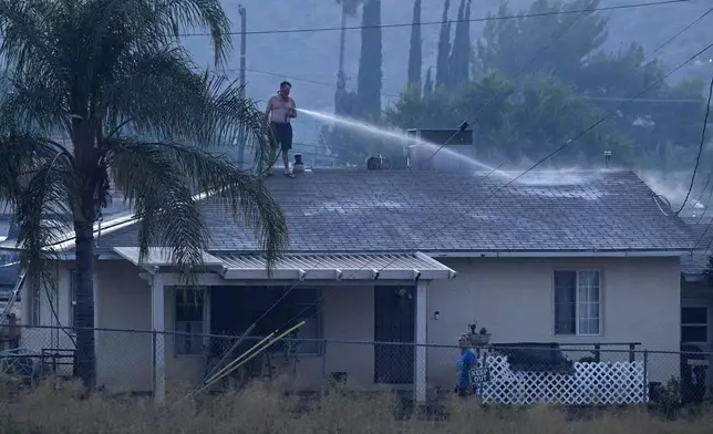 A home owner keeps his roof wet to keep embers from taking hold as Cal Fire Riverside County firefighters battle the Macy Fire in Lake Elsinore, Calif., on Thursday, July 25, 2024. (Terry Pierson/The Orange County Register via AP)