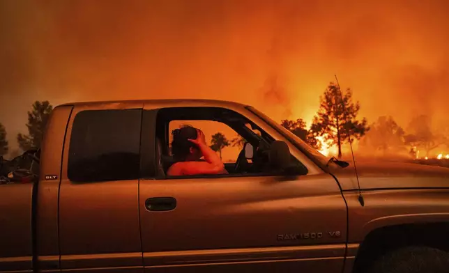 Andrea Douglas holds her head while evacuating as the Park Fire jumps Highway 36 near Paynes Creek in Tehama County, Calif., on Friday, July 26, 2024. (AP Photo/Noah Berger)