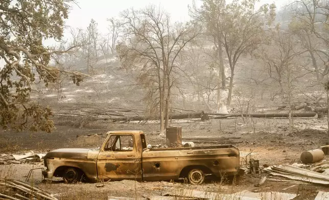 A charred vehicle rests below a hill in Paynes Creek after the Park Fire burned through the community in Tehama County, Calif., on Saturday, July 27, 2024. (AP Photo/Noah Berger)