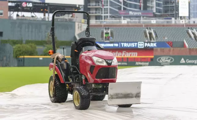 A tractor is placed on a tarp during the rain delay of a baseball game between the Atlanta Braves and the St. Louis Cardinals, Friday, July 19, 2024, in Atlanta. (AP Photo/Jason Allen)