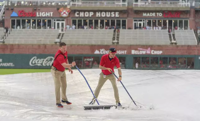 Field staff push rainwater off of a tarp over the infield during the rain delay of a baseball game between the Atlanta Braves and the St. Louis Cardinals, Friday, July 19, 2024, in Atlanta. (AP Photo/Jason Allen)