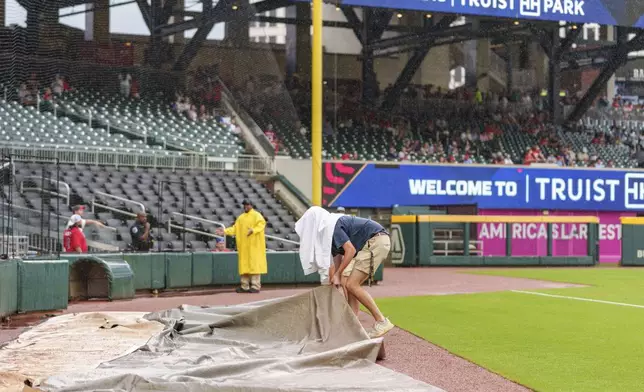 Filed staff pulls a tarp out during the rain delay at a baseball game between the Atlanta Braves and the St. Louis Cardinals, Friday, July 19, 2024, in Atlanta. (AP Photo/Jason Allen)