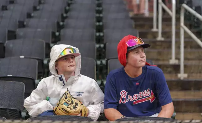 Fans look at the scoreboard for updates during a rain delay of a baseball game between the Atlanta Braves and the St. Louis Cardinals, Friday, July 19, 2024, in Atlanta. (AP Photo/Jason Allen)