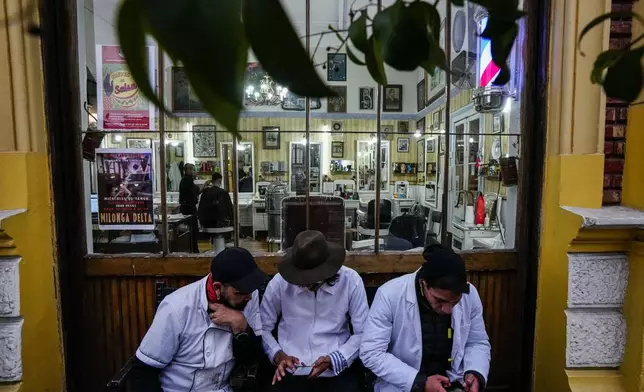 Barbers from the "Peluqueria Francesa" or French Hair Salon, sit outside their workplace in the Yungay neighborhood of Santiago, Chile, June 6, 2024. Yungay is a neighborhood with a mix of historic buildings, baroque facades and modern restaurants, and has also become a popular spot for the homeless. (AP Photo/Esteban Felix)