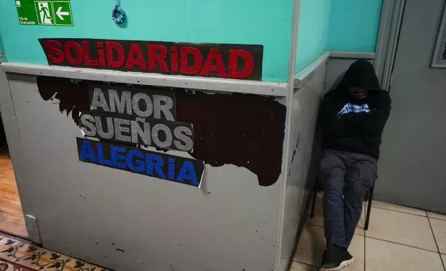 A homeless man rests at the entrance to the shelter "Hogar de Cristo," or Christ's Home in Santiago, Chile, Wednesday, May 15, 2024. The words in Spanish read "Solidarity. Love. Dreams. Joy." (AP Photo/Esteban Felix)