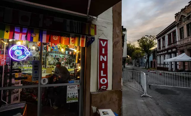 Store workers talk inside a vinyl record shop in the Yungay neighborhood of Santiago, Chile, June 6, 2024. A shelter for the homeless is located on the same block, and the presidential residence is across the street, where metal barriers are set up to block cars. (AP Photo/Esteban Felix)