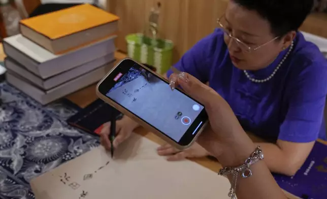 A student uses a smartphone to film Xu Yan, an author of a textbook on nüshu, a centuries-old secret script, demonstrating to write nüshu calligraphy at her studio in Beijing on July 11, 2024. (AP Photo/Andy Wong)