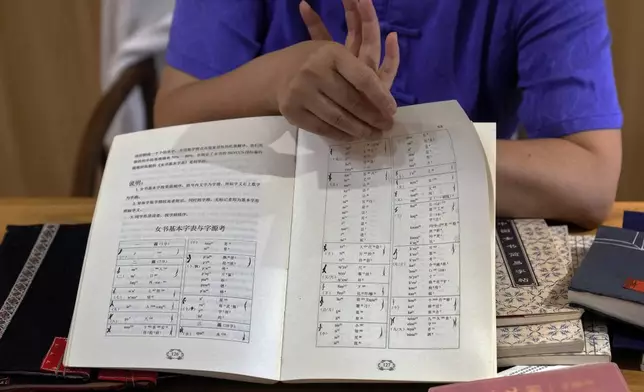 Xu Yan, an author of a textbook on nüshu, a centuries-old secret script, shows a book of nüshu calligraphy to the visiting university students at her studio in Beijing on July 11, 2024. (AP Photo/Andy Wong)