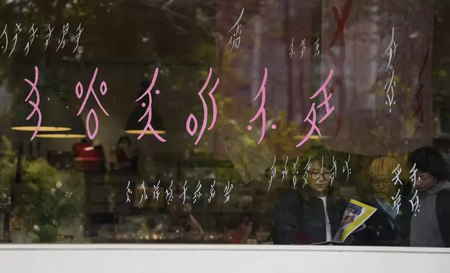 Visitors to a bookstore specializing in nüshu, a centuries-old secret script, browse materials, behind the window with nüshu writing in Chengdu in southwestern China's Sichuan province, March 17, 2024. (AP Photo/Ng Han Guan)