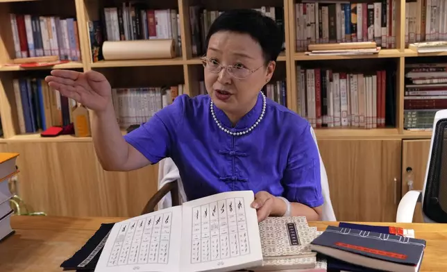 Xu Yan, an author of a textbook on nüshu, a centuries-old secret script, shows a book of nüshu calligraphy to the visiting university students at her studio in Beijing on July 11, 2024. (AP Photo/Andy Wong)