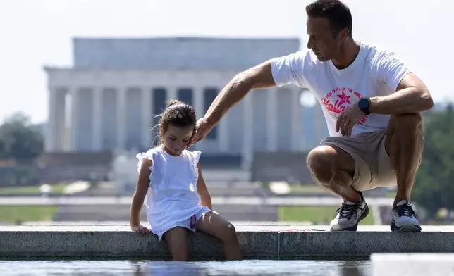 FILE - Andrea Di Miele, right, from Hoboken, N.J., puts water on his daughter, Sofia Di Miele, 10, with the Lincoln Memorial behind, June 21, 2024, in Washington. Temperatures are forecast to reach 100 degrees on Saturday. June 2024 was the hottest June on record, according to Europe's Copernicus climate service on Monday, July 8. (AP Photo/Alex Brandon, File)