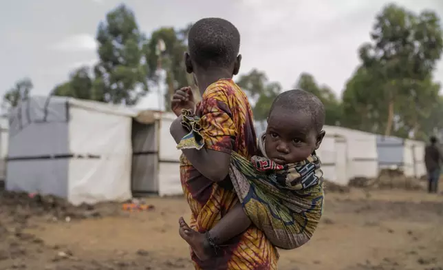 A young girl carrying her sister on her back stand outside a refugee camp on the outskirts of Goma, Democratic Republic of the Congo, Thursday, July 11, 2024. The top U.N. official in Congo on Monday welcomed a two-week humanitarian cease-fire in its mineral-rich east, where she said violence has reached "alarming levels" and risked provoking a wider regional conflict. (AP Photo/Moses Sawasawa)