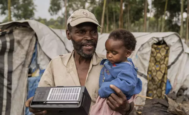 A man holds his child while listening to the radio at a refugee camp on the outskirts of Goma, Democratic Republic of the Congo, Thursday, July 11, 2024. The top U.N. official in Congo on Monday welcomed a two-week humanitarian cease-fire in its mineral-rich east, where she said violence has reached "alarming levels" and risked provoking a wider regional conflict. (AP Photo/Moses Sawasawa)