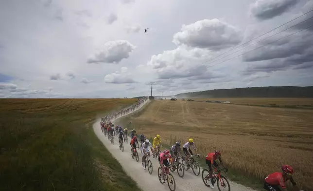 The pack with Slovenia's Tadej Pogacar, wearing the overall leader's yellow jersey, and Netherlands' Mathieu van der Poel, left of Pogacar in white, rides on a gravel road during the ninth stage of the Tour de France cycling race over 199 kilometers (123.7 miles) with start and finish in Troyes, France, Sunday, July 7, 2024. (AP Photo/Daniel Cole)