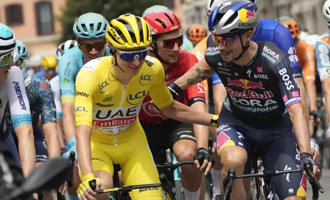 Slovenia's Tadej Pogacar, wearing the overall leader's yellow jersey, and Slovenia's Primoz Roglic talk during the ceremonial parade of the third stage of the Tour de France cycling race over 230.8 kilometers (143.4 miles) with start in Piacenza and finish in Turin, Italy, Monday, July 1, 2024. Right is Belgium's Remco Evenepoel, wearing the best young rider's white jersey. (AP Photo/Jerome Delay)