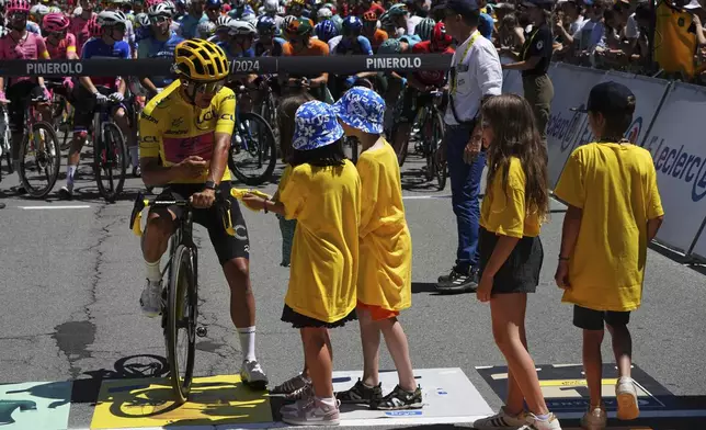 Ecuador's Richard Carapaz, wearing the overall leader's yellow jersey, talk with cycling fans as he waits for the start of the fourth stage of the Tour de France cycling race over 139.6 kilometers (86.7 miles) with start in Pinerolo, Italy and finish in Valloire, France, Tuesday, July 2, 2024. (AP Photo/Daniel Cole)