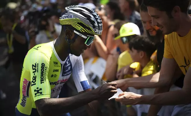 Eritrea's Biniam Girmay signs autographs prior to the start of the second stage of the Tour de France cycling race over 199.2 kilometers (123.8 miles) with start in Cesenatico and finish in Bologna, Italy, Sunday, June 30, 2024. (AP Photo/Daniel Cole)
