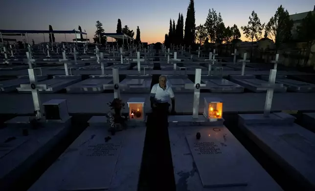 Loucas Alexandrou, 94, seats by the grave, right, of his son Christakis Alexandrou, Alexandrides, who where killed on 22 of July 1974 during the Turkish invasion, at the military cemetery in the divided capital Nicosia, Cyprus, Friday, July 19, 2024. Saturday marks the 50th anniversary of Cyprus' ethnic division after Turkish invaded in the summer of 1974 in the wake of an Athens junta-backed coup aiming at union with Greece. (AP Photo/Petros Karadjias)