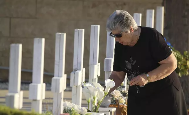 A relative of a soldier, killed in the 1974 Turkish invasion of Cyprus, lights a candle at a grave in the Tymvos Macedonitissas military cemetery during the 50th anniversary in the divided capital of Nicosia, Cyprus, Saturday, July 20, 2024. Saturday marks the 50th anniversary of Cyprus' ethnic division after Turkish invaded in the summer of 1974 in the wake of an Athens junta-backed coup aiming at union with Greece. (AP Photo/Philippos Christou)