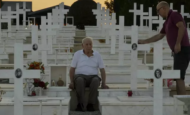 Loucas Alexandrou, 94, and his younger son Vassos Alexandrou, 61, right, are seen by the grave of his son, and brother, of Christakis Alexandrou, Alexandrides, who was killed on July 22, 1974 during the Turkish invasion, at the military cemetery in the divided capital Nicosia, Cyprus, Friday, July 19, 2024. Saturday marks the 50th anniversary of Cyprus' ethnic division after Turkish invaded in the summer of 1974 in the wake of an Athens junta-backed coup aiming at union with Greece. (AP Photo/Petros Karadjias)