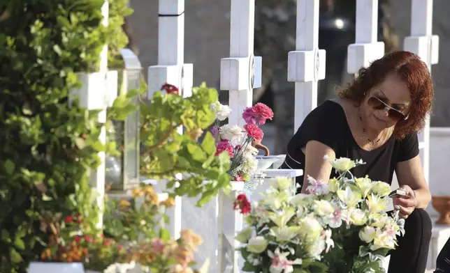 A woman leaves flowers on the graves of soldiers, killed in the 1974 Turkish invasion in Cyprus, at the Tymvos Macedonitissas military cemetery in the divided capital of Nicosia Cyprus, Saturday, July 20, 2024. Saturday marks the 50th anniversary of Cyprus' ethnic division after Turkish invaded in the summer of 1974 in the wake of an Athens junta-backed coup aiming at union with Greece. (AP Photo/Philippos Christou)