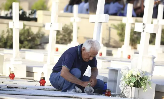 A relative of a soldier, killed in the 1974 Turkish invasion of Cyprus, lights a candle at a grave in the Tymvos Macedonitissas military cemetery during the 50th anniversary in the divided capital of Nicosia, Cyprus, Saturday, July 20, 2024. Saturday marks the 50th anniversary of Cyprus' ethnic division after Turkish invaded in the summer of 1974 in the wake of an Athens junta-backed coup aiming at union with Greece. (AP Photo/Philippos Christou)