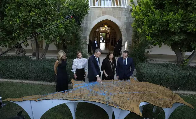 Cyprus' President Nikos Christodoulides, right, with his wife Philippa Karsera, second left, Greek Prime Minister Kyriakos Mitsotakis, center, his wife Mareva Grabowski-Mitsotakis, left, and Cypriot Deputy minister of culture Vasiliki Kasianidou, center right, look an art work "NEMATA" showing the Cyprus island, at the presidential palace in the divided capital Nicosia, Cyprus, Saturday, July 20, 2024. Greek Cypriot commemorations include the unveiling of memorials to fallen heroes, church services and a gathering late Saturday at the Presidential Palace addressed — for the first time — by Greek Prime Minister Kyriakos Mitsotakis. (AP Photo/Petros Karadjias)