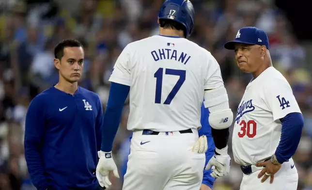 Los Angeles Dodgers designated hitter Shohei Ohtani, front center, speaks with interpreter Will Ireton, head athletic trainer Thomas Albert, and manager Dave Roberts, from left, after being hit by a foul tip during the third inning of a baseball game against the Arizona Diamondbacks, Tuesday, July 2, 2024, in Los Angeles. (AP Photo/Ryan Sun)