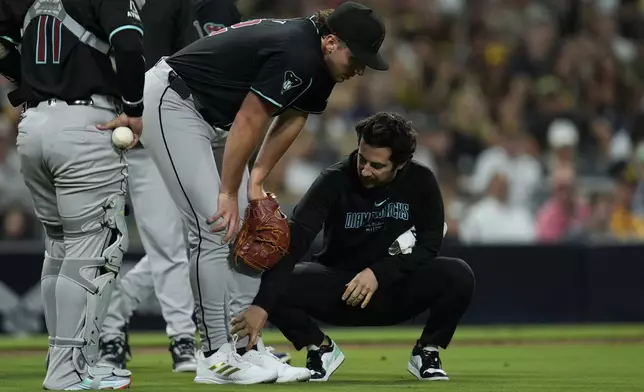 Arizona Diamondbacks starting pitcher Brandon Pfaadt, center, leans over as a trainer looks at his leg after an injury during the fifth inning of a baseball game against the San Diego Padres, Saturday, July 6, 2024, in San Diego. (AP Photo/Gregory Bull)