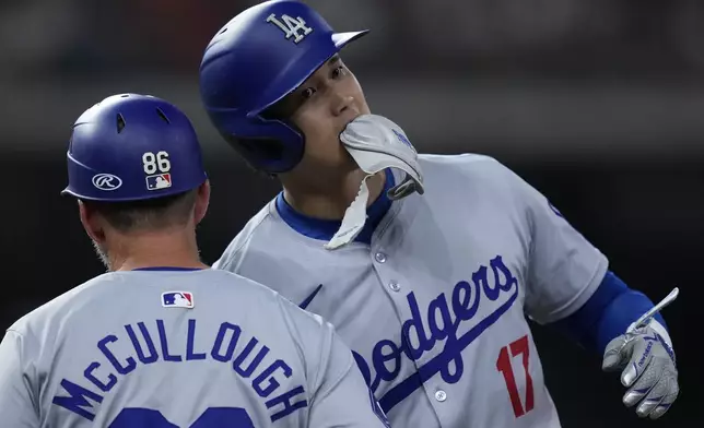 Los Angeles Dodgers designated hitter Shohei Ohtani, right, bumps helmets with first base coach Clayton McCullough, left, after a base hit during the eighth inning of a baseball game against the Houston Astros, Friday, July 26, 2024, in Houston. (AP Photo/Kevin M. Cox)