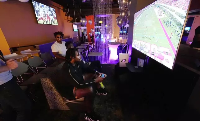 Colorado center Yakiri Walker, front, and running back Kam Mikell, center, join offensive lineman Tyler Johnson, left, in playing the EA Sports College Football 25 video game during a release party Friday, July 19, 2024, at the Memorial Union on the campus of the University of Colorado in Boulder, Colo. EA Sports College Football 25 flooded the market Friday as gamers who waited more than a decade for the franchise's next installment hurry to play. (AP Photo/David Zalubowski)