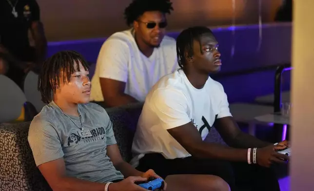 Colorado wide receiver Kaleb Mathis, left, faces off against running back Kam Mikell, right, as offensive lineman Tyler Johnson looks on during the EA Sports College Football 25 video game release party Friday, July 19, 2024, at the Memorial Union at University of Colorado in Boulder, Colo. (AP Photo/David Zalubowski)