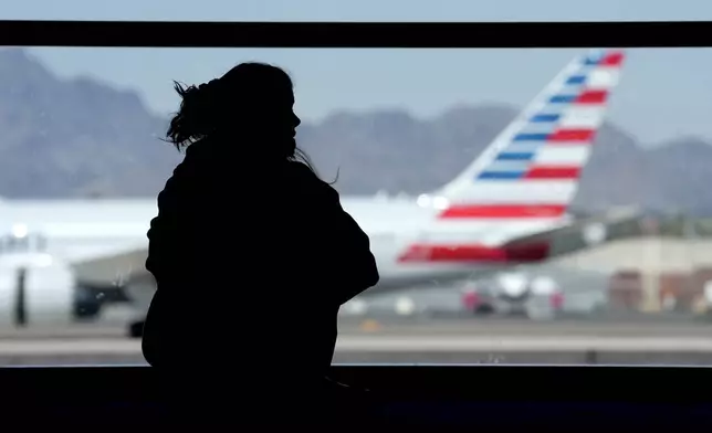 FILE - A woman waits for her flight as an American Airlines jet passes by at Sky Harbor airport on March 4, 2023, in Phoenix. American reports earnings on Thursday, July 25, 2024. (AP Photo/Charlie Riedel, File)