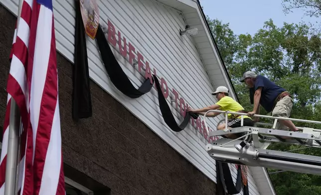 Logan Check, left, junior firefighter, and Randy Reamer, president and rescue captain at the Buffalo Township Fire Company 27, hang bunting on the fire station in memory of fellow firefighter Corey Comperatore, in Buffalo Township, Pa., Sunday, July 14, 2024. Comperatore was killed during a shooting at a campaign rally for Republican presidential candidate former President Donald Trump in Butler, Pa., on Saturday. The flag at the station house flies at half staff at left. (AP Photo/Sue Ogrocki)