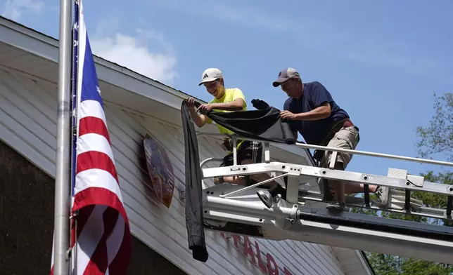 Logan Check, left, junior firefighter, and Randy Reamer, right, president and rescue captain at the Buffalo Township Fire Company 27, hang bunting on the fire station in memory of fellow firefighter Corey Comperatore, in Buffalo Township, Pa., Sunday, July 14, 2024. Comperatore was killed during a shooting at a campaign rally for Republican presidential candidate former President Donald Trump in Butler, Pa., on Saturday. The flag at the station house flies at half staff at left. (AP Photo/Sue Ogrocki)