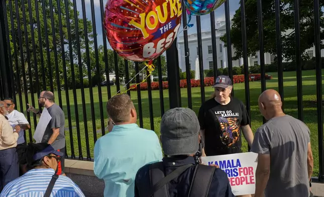 A man who asked not to be named holds balloons in support of President Joe Biden, as Tony Tribby, of Virginia, wears a t-shirt in support of Vice President Kamala Harris, while people gather, Sunday July 21, 2024, outside the White House in Washington. Biden dropped out of the 2024 race for the White House on Sunday, ending his bid for reelection following a disastrous debate with Donald Trump that raised doubts about his fitness for office just four months before the election. (AP Photo/Jacquelyn Martin)