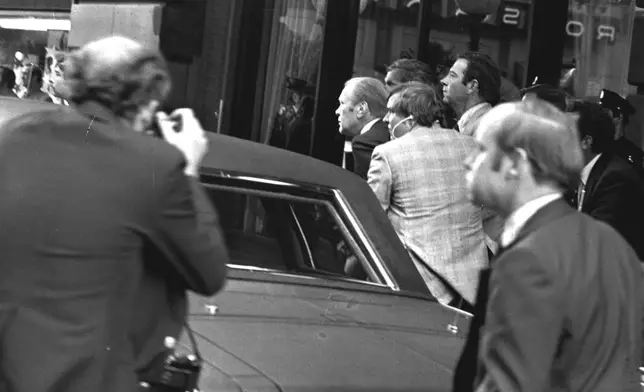 FILE - President Ford ducks behind his limousine and is hustled into the vehicle after a shot was fired as he left the St. Francis Hotel in San Francisco, Sept. 22, 1975. The President was rushed to the airport to return to Washington. (AP Photo, File)
