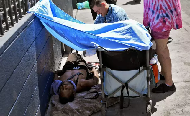 Dr. Matt Essary checks on a homeless man who fell ill on the sidewalk outside one of five Circle The City mobile clinics stationed outside soup kitchens and other services for homeless people, Thursday, May 30, 2024 in Phoenix. Based in the hottest big metro in America, Circle the City is taking measures to protect patients from life-threatening heat illness as temperatures hit new highs. Homeless people accounted for nearly half of the record 645 heat-related deaths last year in Arizona's Maricopa County, which encompasses metro Phoenix.(AP Photo/Matt York)