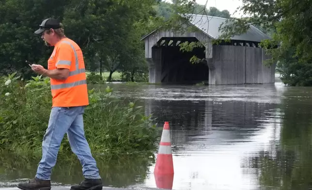 Jody Tanner, of the Vermont Transportation Agency, talks with co-workers at a high water point of the Lamoille River along Route 15 after remnants of Hurricane Beryl caused flooding, Thursday, July 11, 2024, in Cambridge, Vt. At rear is the Gates Farm Covered Bridge. (AP Photo/Charles Krupa)