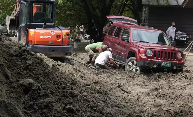 Two men dig out an SUV stuck in the mud along Hudson Avenue after remnants of Hurricane Beryl caused flooding and destruction, Friday, July 12, 2024, in Plainfield, Vt. (AP Photo/Charles Krupa)