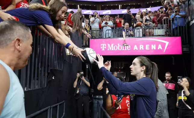 Indiana Fever guard Caitlin Clark autographs a basketball for a fan before a WNBA basketball game between the Las Vegas Aces and the Indiana Fever Tuesday, July 2, 2024, in Las Vegas. (Steve Marcus/Las Vegas Sun via AP)
