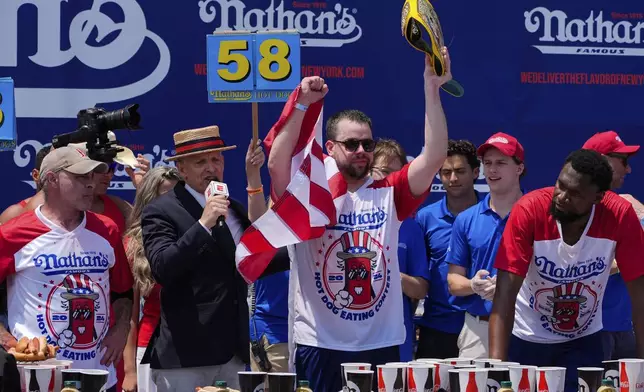 Patrick Bertoletti, center, reacts after winning the men's division in Nathan's Famous Fourth of July hot dog eating contest, Thursday, July 4, 2024, at Coney Island in the Brooklyn borough of New York. Bertoletti ate 58 hot dogs. (AP Photo/Julia Nikhinson)