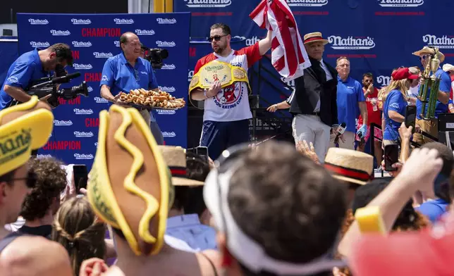 Patrick Bertoletti, center, reacts after winning the men's division in Nathan's Famous Fourth of July hot dog eating contest, Thursday, July 4, 2024, at Coney Island in the Brooklyn borough of New York. Bertoletti ate 58 hot dogs. (AP Photo/Julia Nikhinson)
