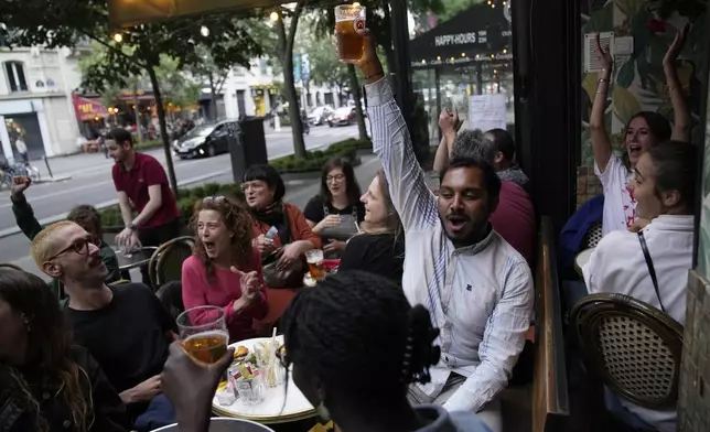 People react to the projection of results during the second round of the legislative elections, near Republique Plaza in Paris, France. Polls have closed in France, and polling projections say a coalition on the left that came together unexpectedly has won the most parliamentary seats in the pivotal runoff elections after a high turnout among voters.(AP Photo/Christophe Ena)