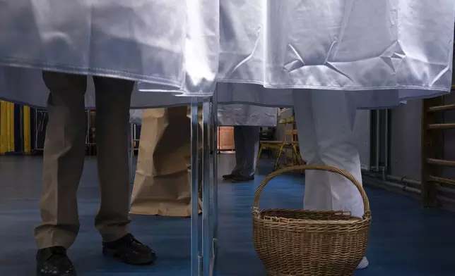 Voters stand in the polling booth during the second round of the legislative elections, Sunday, July 7, 2024 in Paris. France votes Sunday in pivotal runoff elections that could hand a historic victory to Marine Le Pen's far-right National Rally and its inward-looking, anti-immigrant vision — or produce a hung parliament and years of political deadlock. (AP Photo/Louise Delmotte)