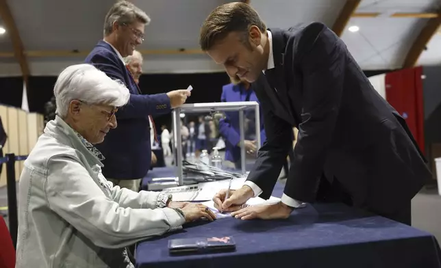 French President Emmanuel Macron, right, signs after voting for the second round of the legislative elections in Le Touquet-Paris-Plage, northern France, Sunday July 7 2024. Voting has begun in mainland France on Sunday in pivotal runoff elections that could hand a historic victory to Marine Le Pen's far-right National Rally and its inward-looking, anti-immigrant vision — or produce a hung parliament and political deadlock. (Mohammed Badra, Pool via AP)