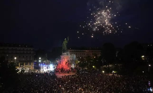 Fireworks go off as people stand in Republique Plaza and react to the projection of results during the second round of the legislative elections, in Paris, France. Polls have closed in France, and polling projections say a coalition on the left that came together unexpectedly has won the most parliamentary seats in the pivotal runoff elections after a high turnout among voters. (AP Photo/Christophe Ena)